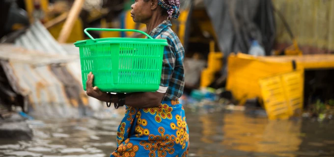 Woman walking in a flooded environment, carrying a green plastic basket. 