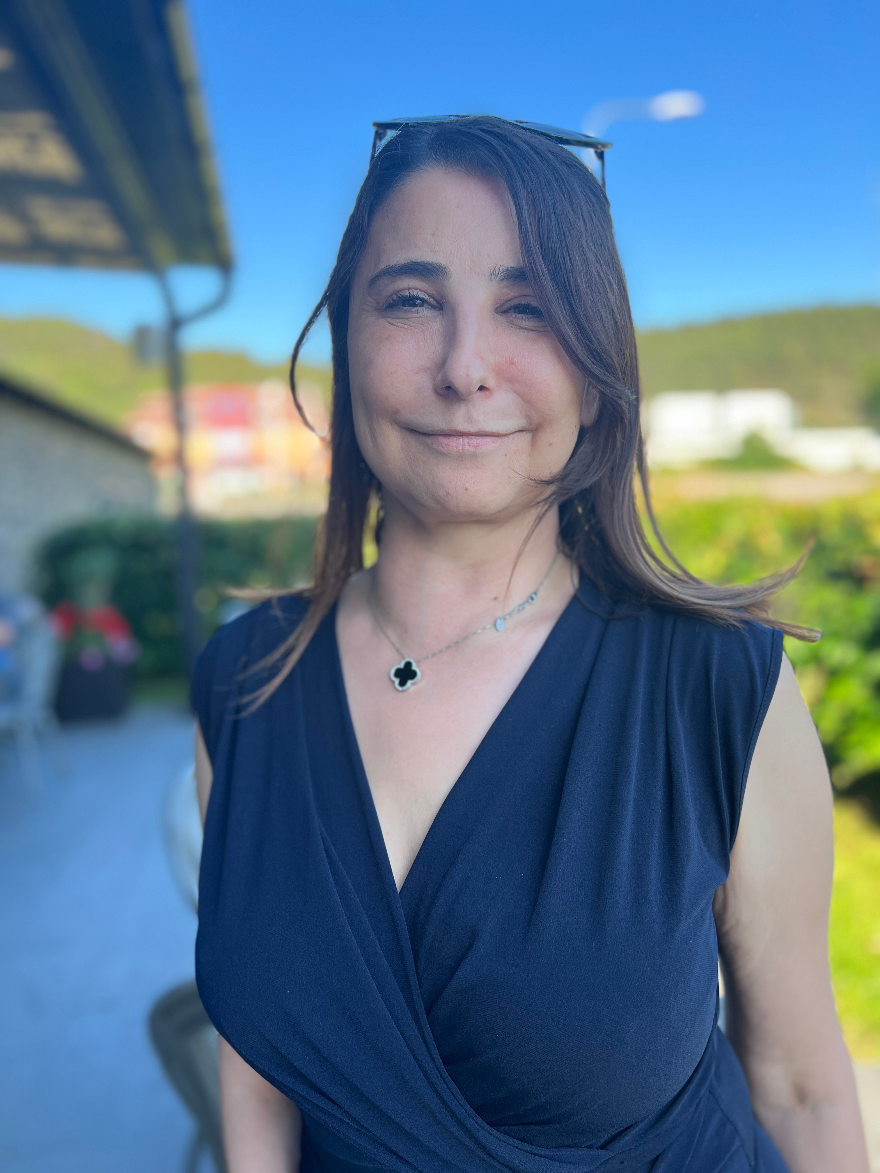 Leende person i mörkblå ärmlös topp står utomhus med grönskande kullar i bakgrunden.