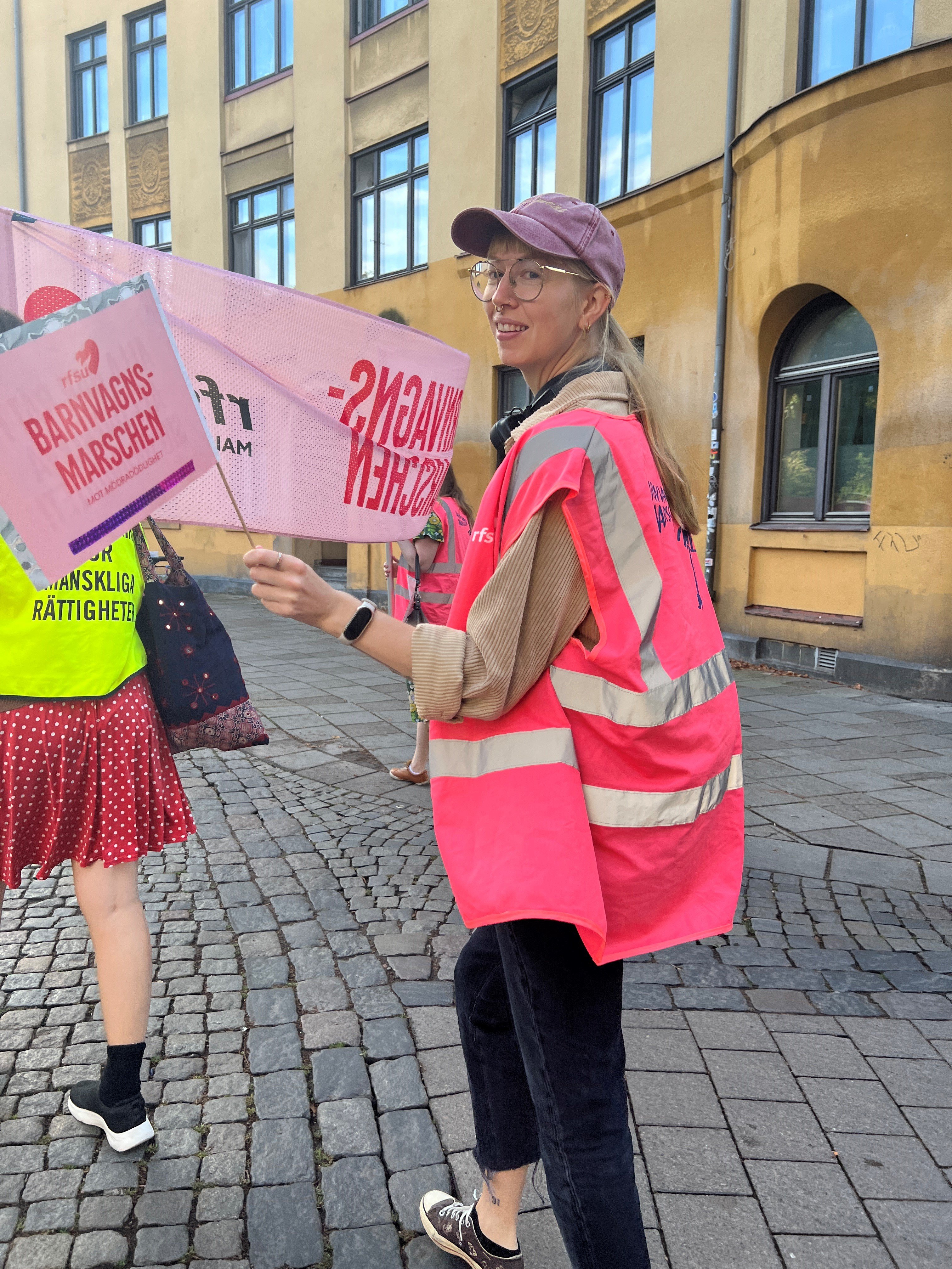 En kvinna går på demonsration med skyltar i handen och keps