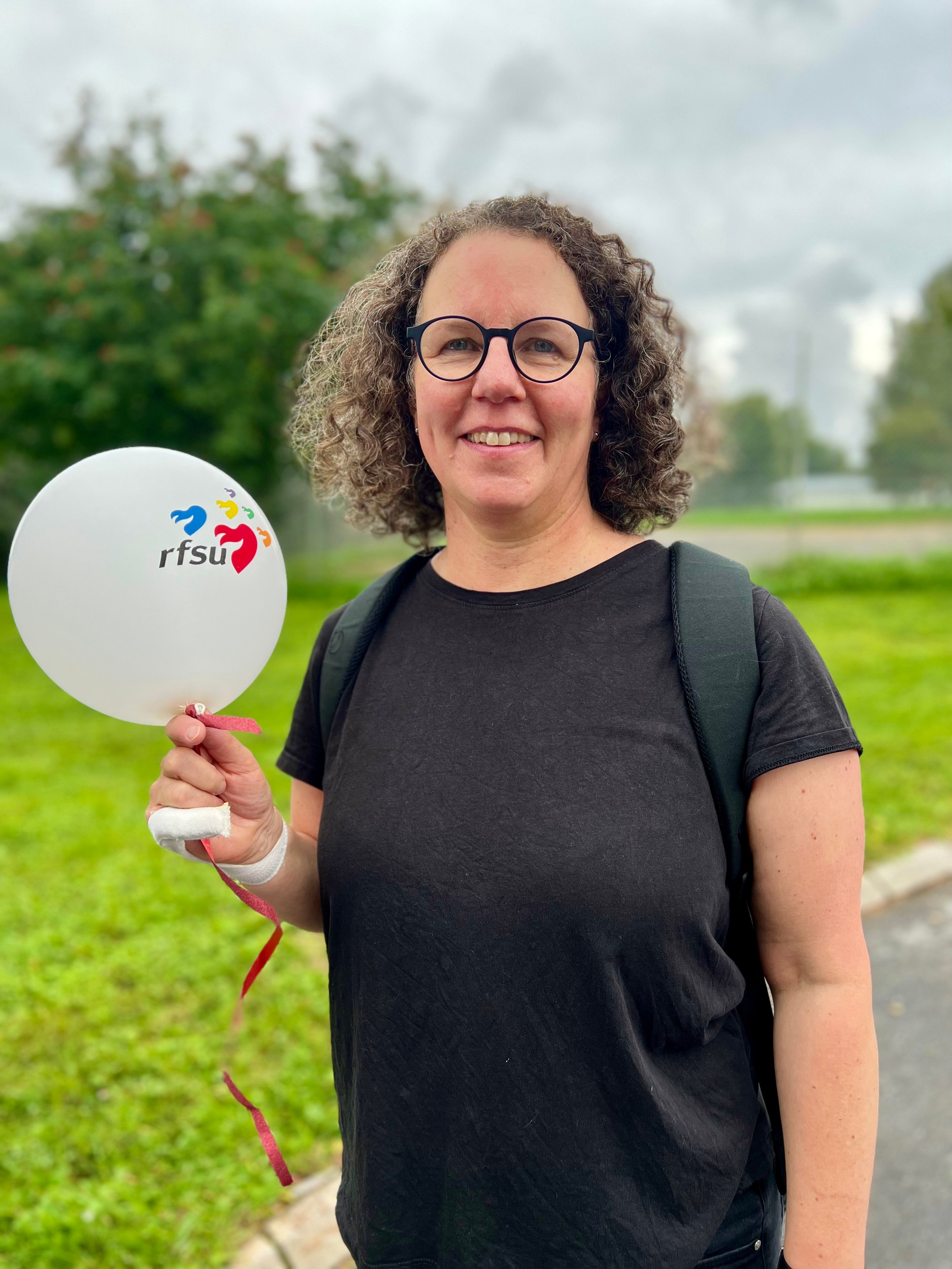 Person i lockigt hår och glasögon håller upp en RFSU-ballong. 