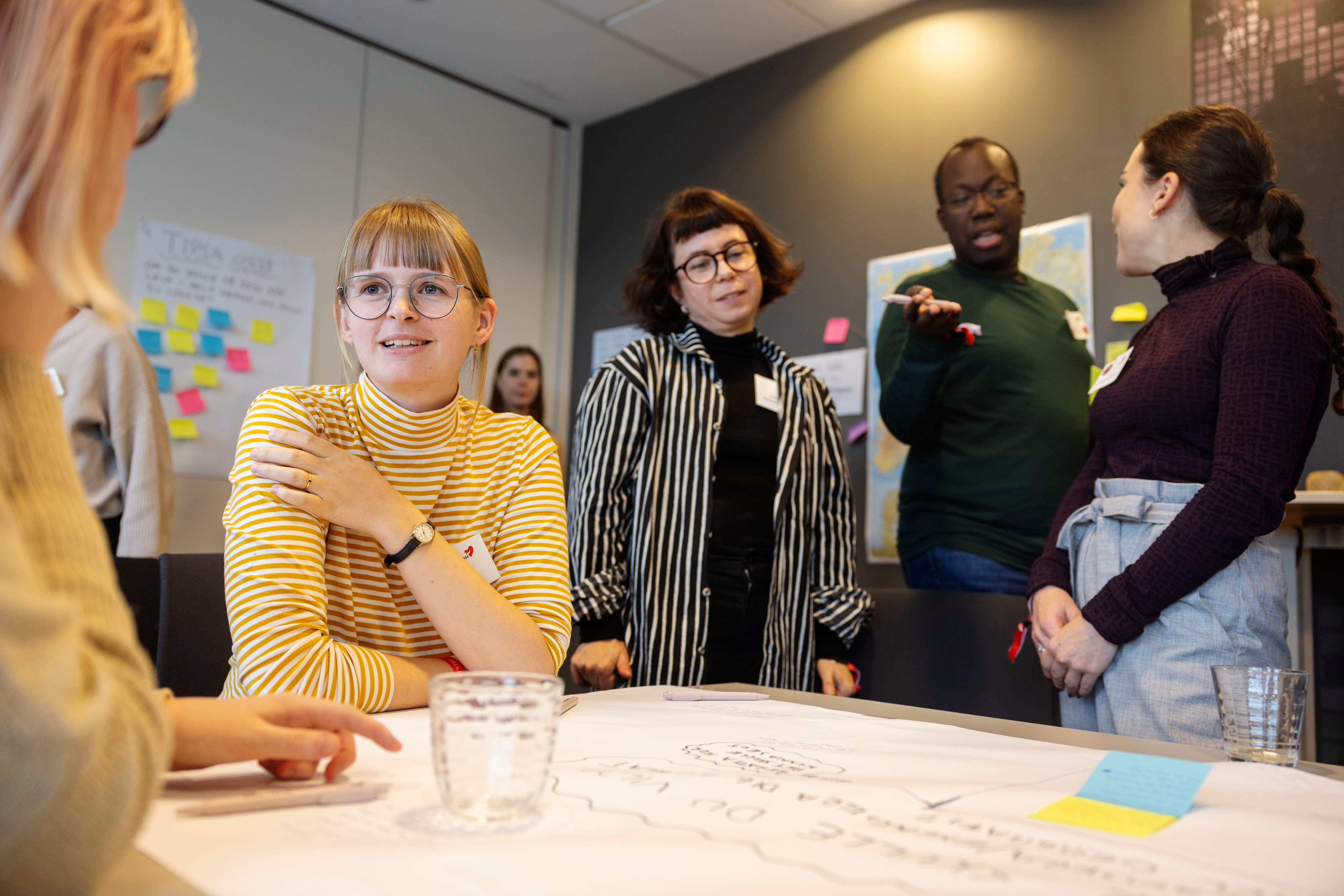 Fyra deltagare i ett djupt samtal runt ett arbetsbord täckt med blädderblockspapper och post-it-lappar.