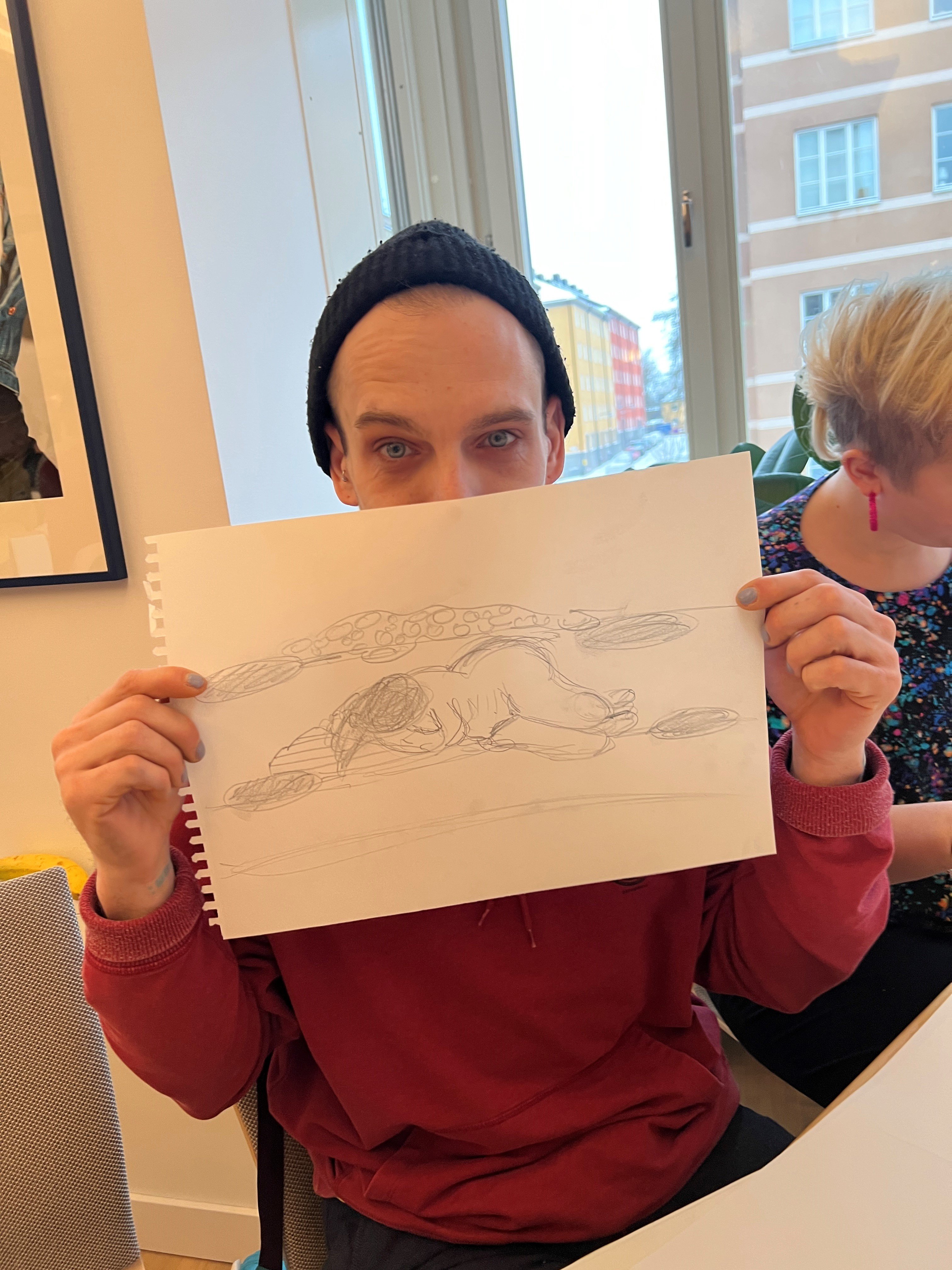 En person håller upp en teckning som föreställer en liggande gestalt framför sitt ansikte.