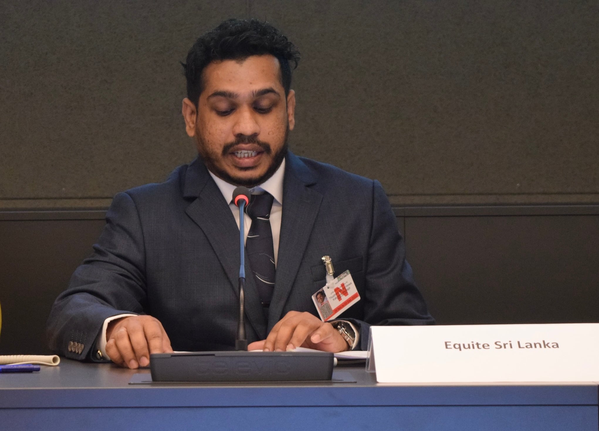 Person i kostym talar i mikrofon vid bordet märkt Equite Sri Lanka.