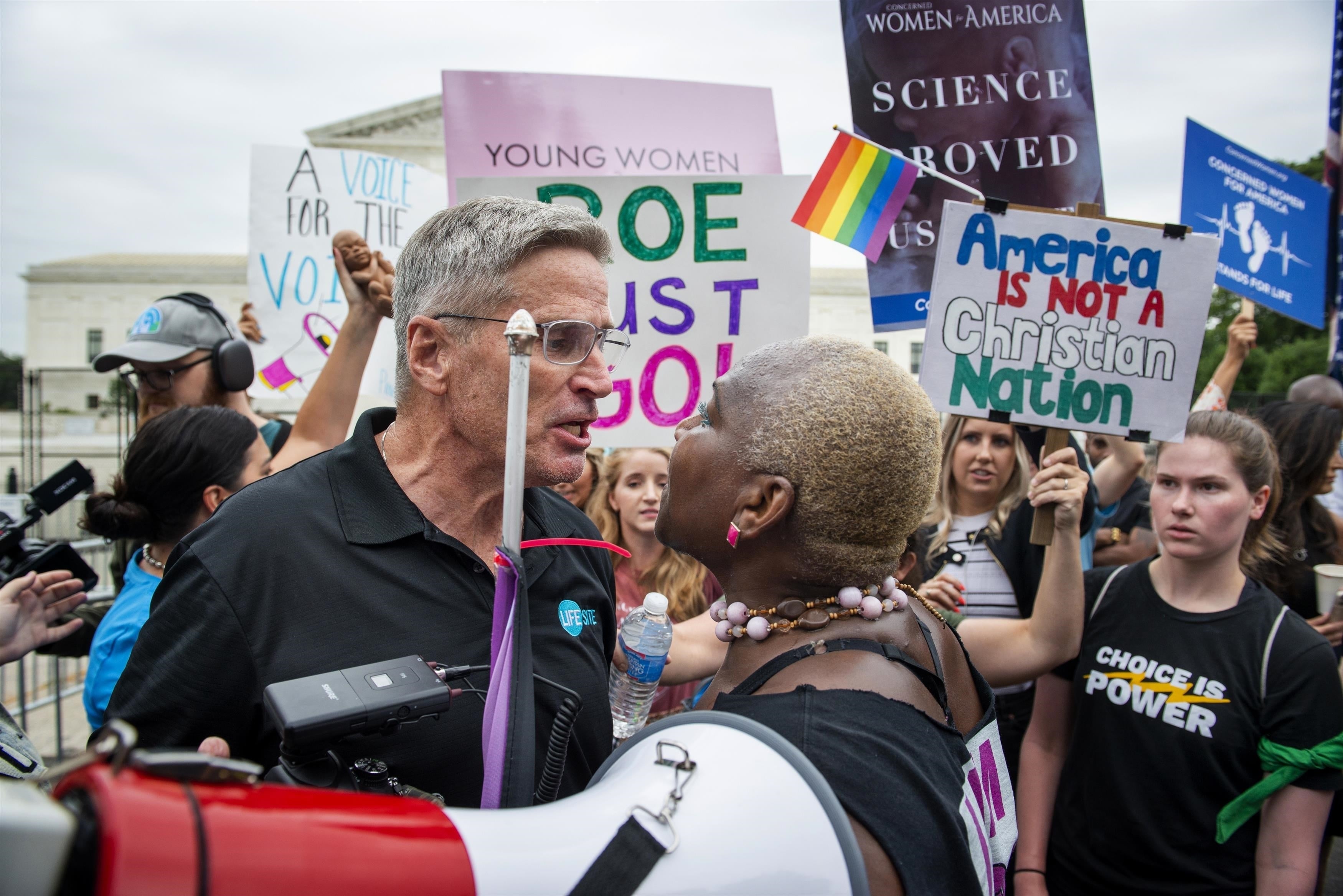 En intensiv konfrontation ansikte mot ansikte mellan en man och en kvinna under en demonstration med olika protestskyltar utanför USA:s högsta domstol.