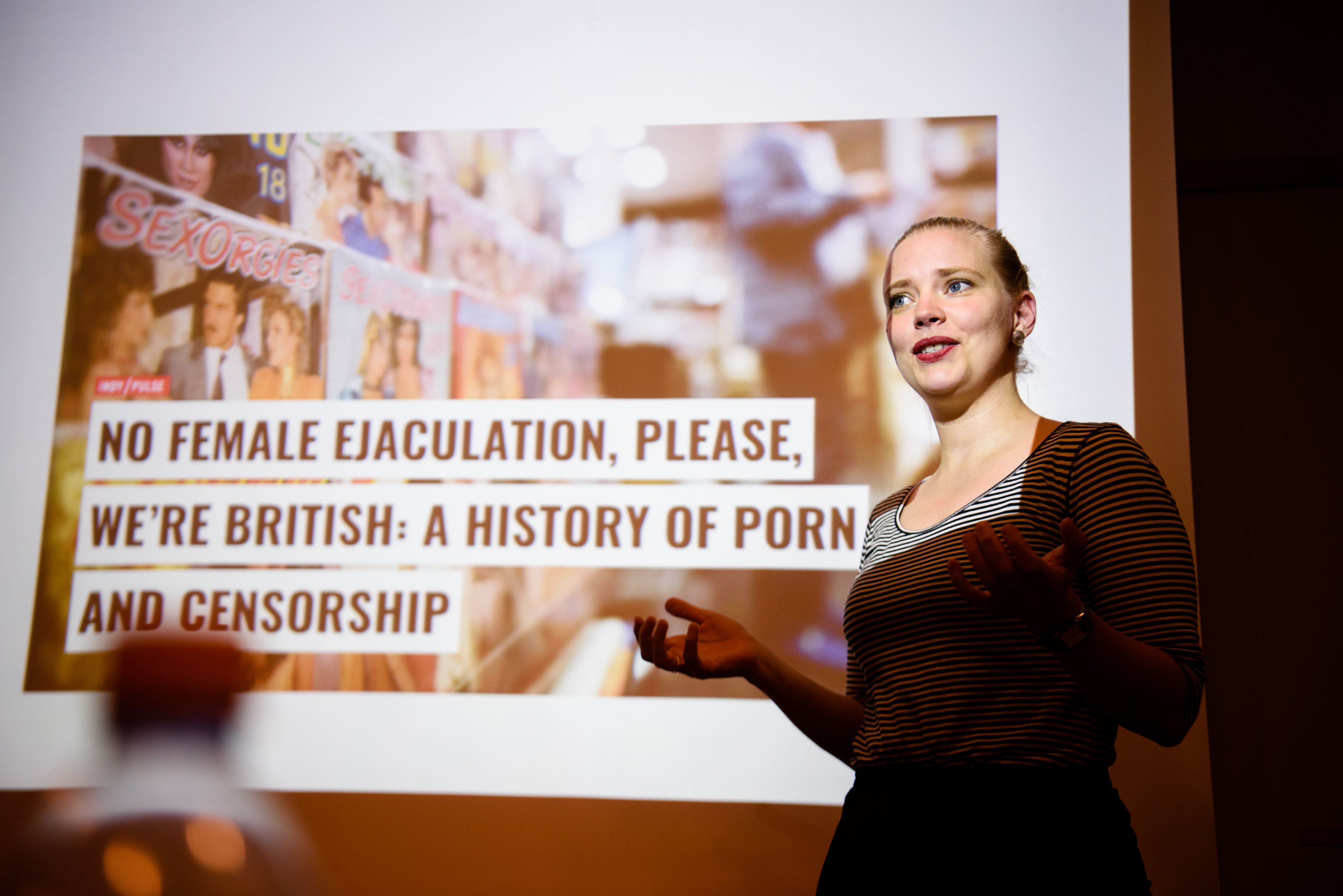 En kvinna föreläser framför en projektorskärm med texten "A History of Porn and Censorship".
