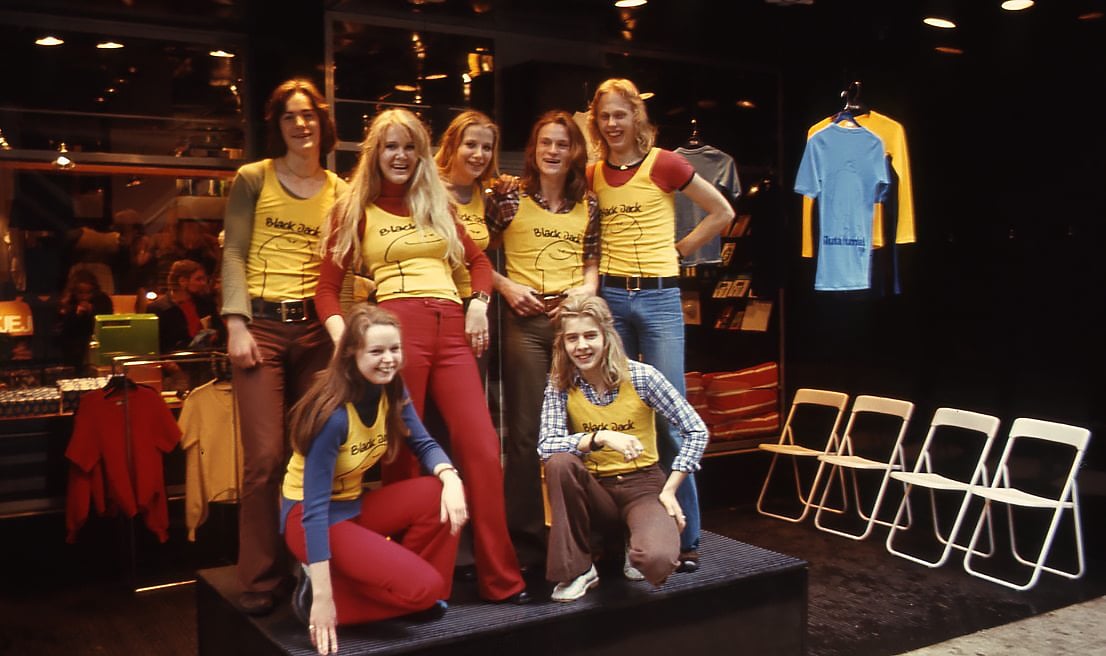 Ett gäng ungdomar i 70-talsfrisyrer poserar med gula linnen som det står Black Jack på. 