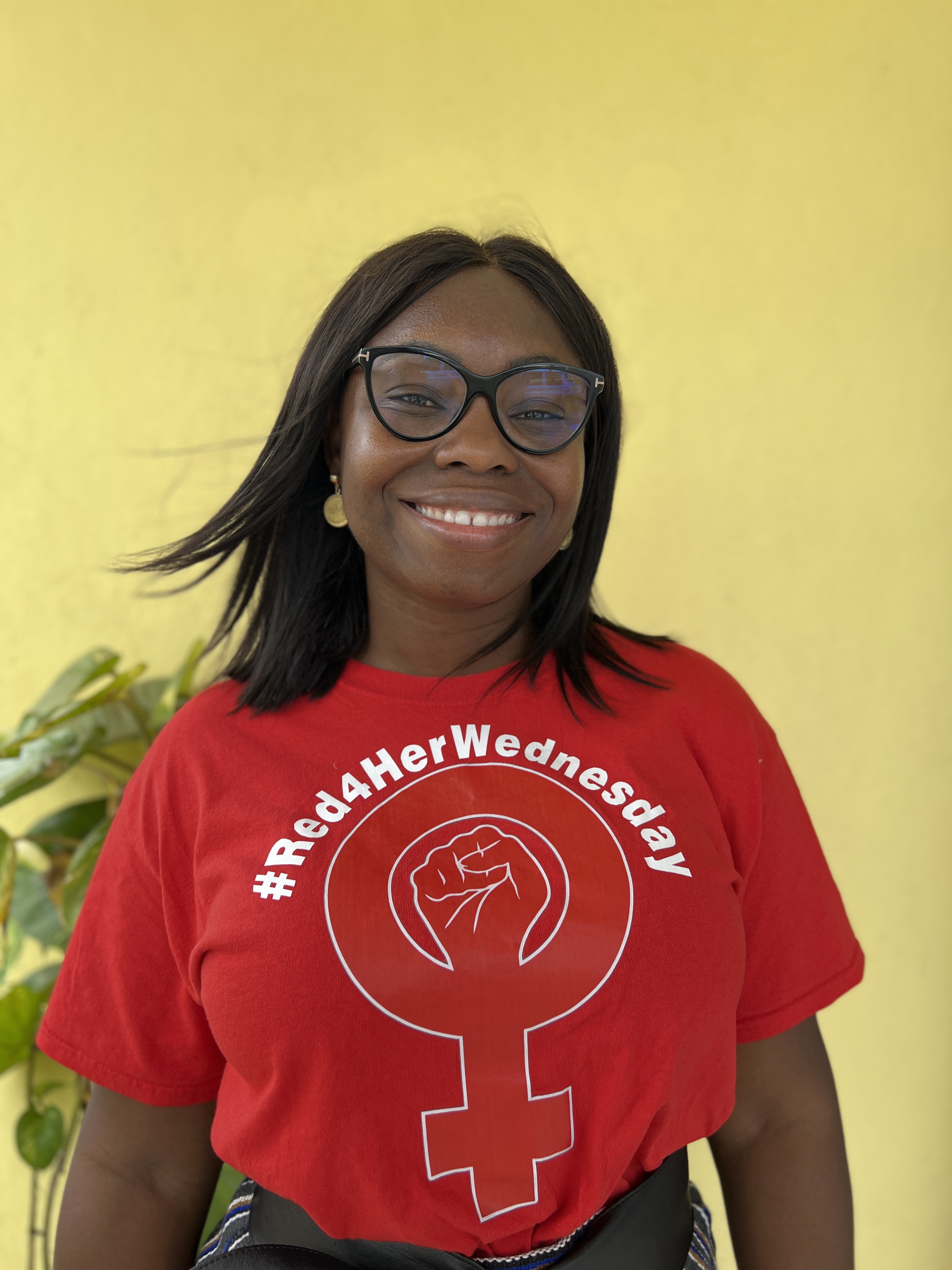 A woman with glasses and red t-shirt smiles to the camera.