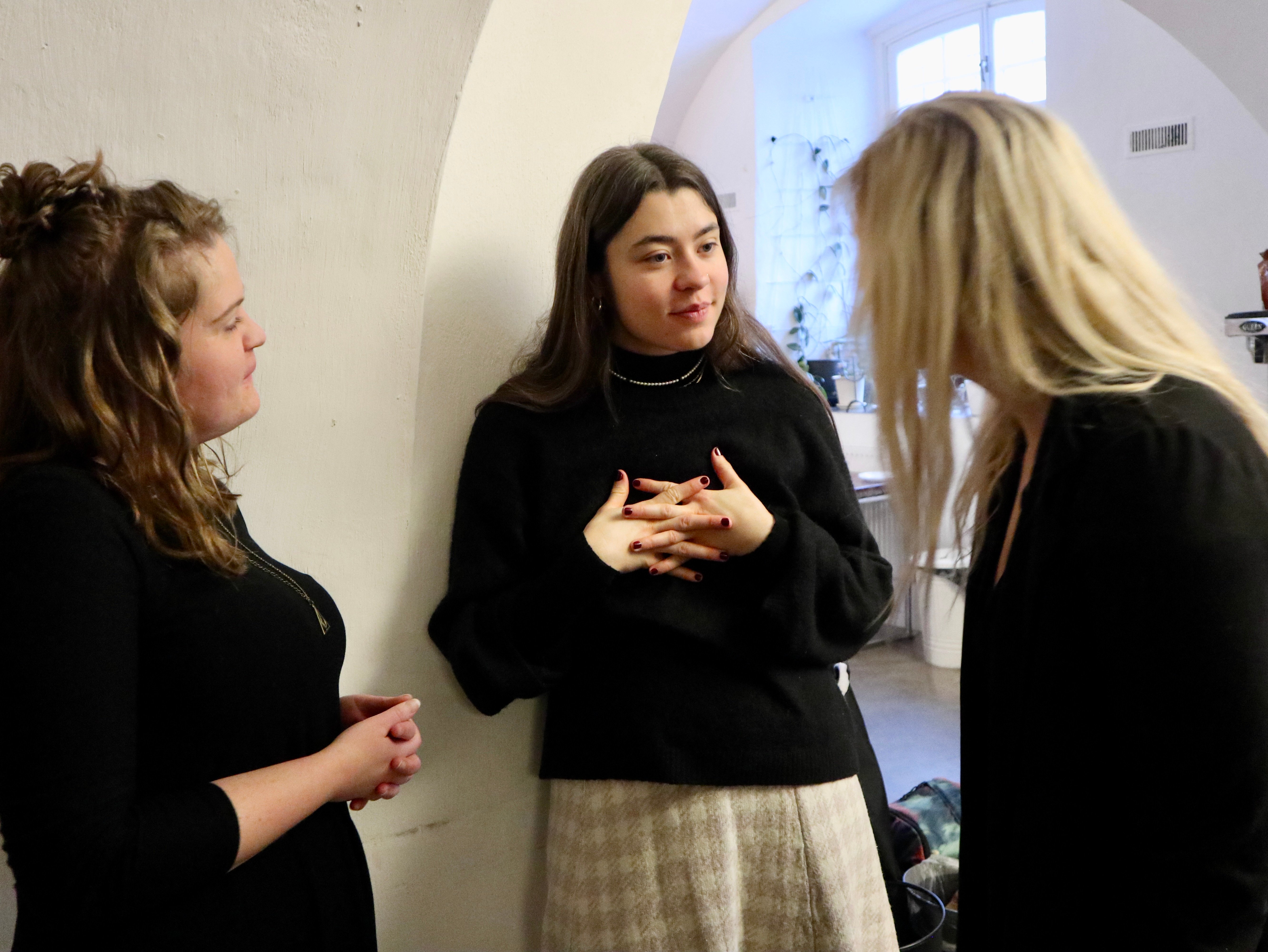 Tre personer står nära varandra och för ett engagerat samtal i en ljus lokal.