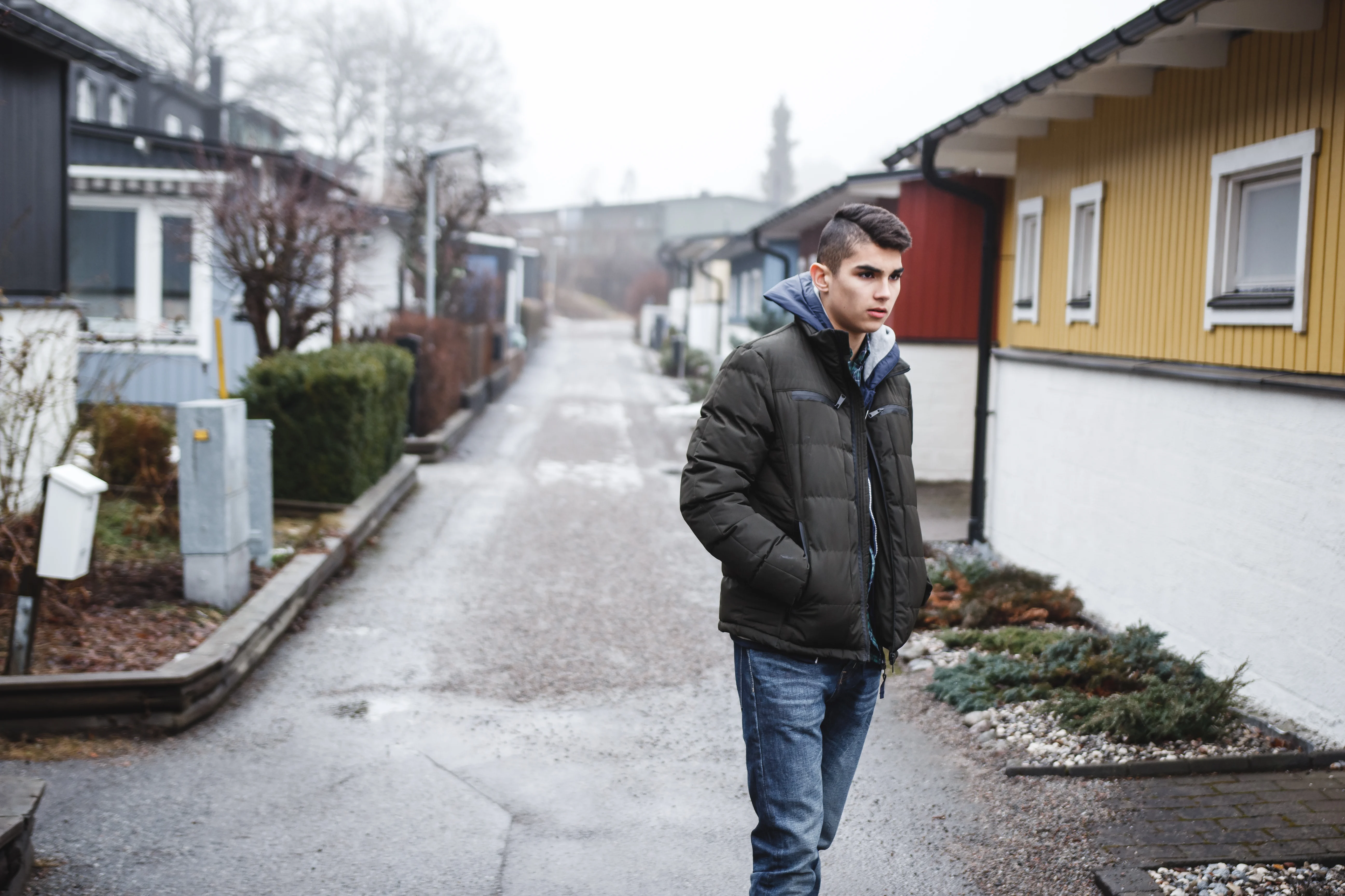 En tonåring med kort svart hår, jeans och grå dunjacka står mellan färgglada hus
