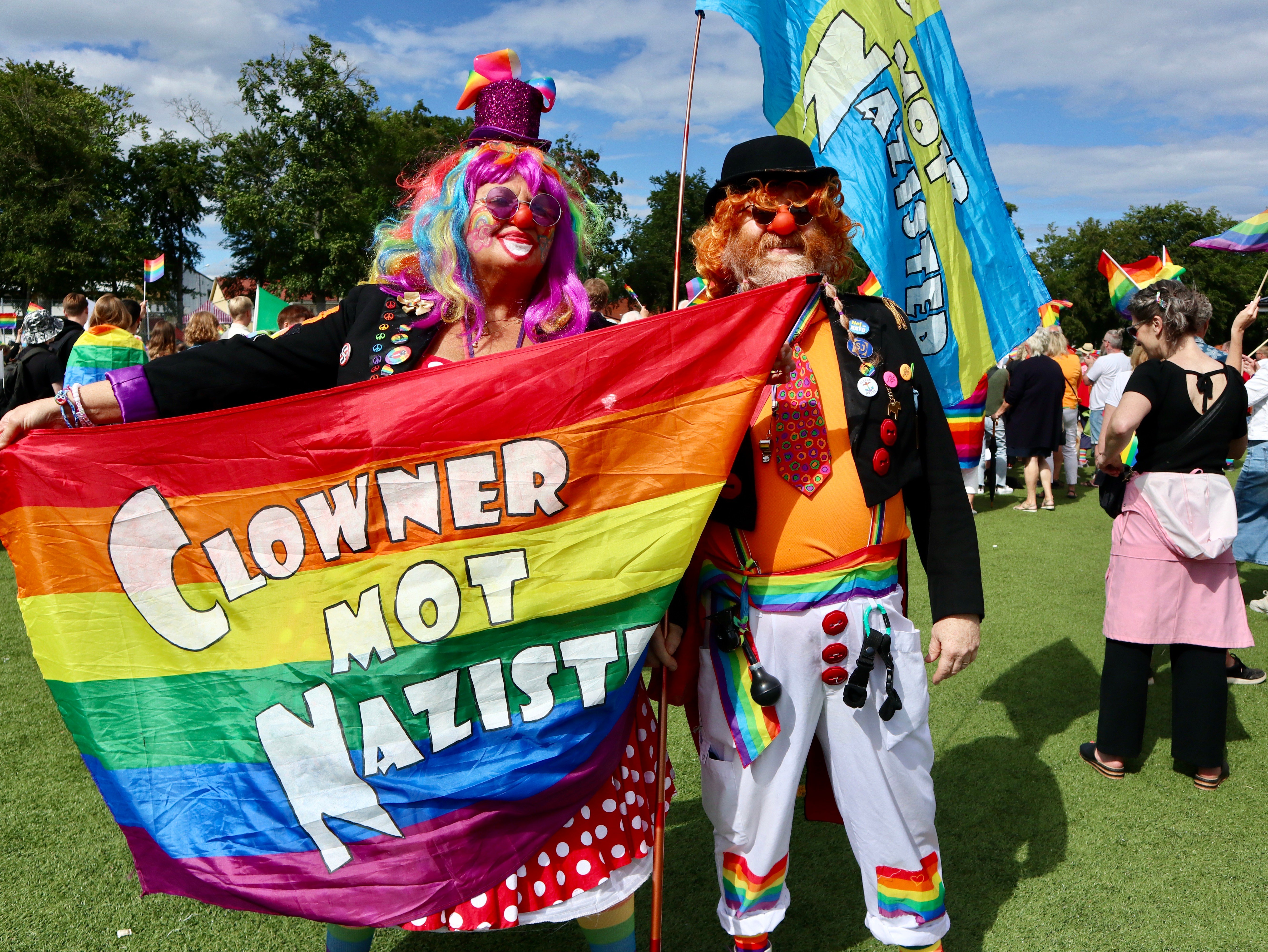 Två personer utklädda till clowner håller upp en stor regnbågsflagga med texten "Clowner mot nazister".