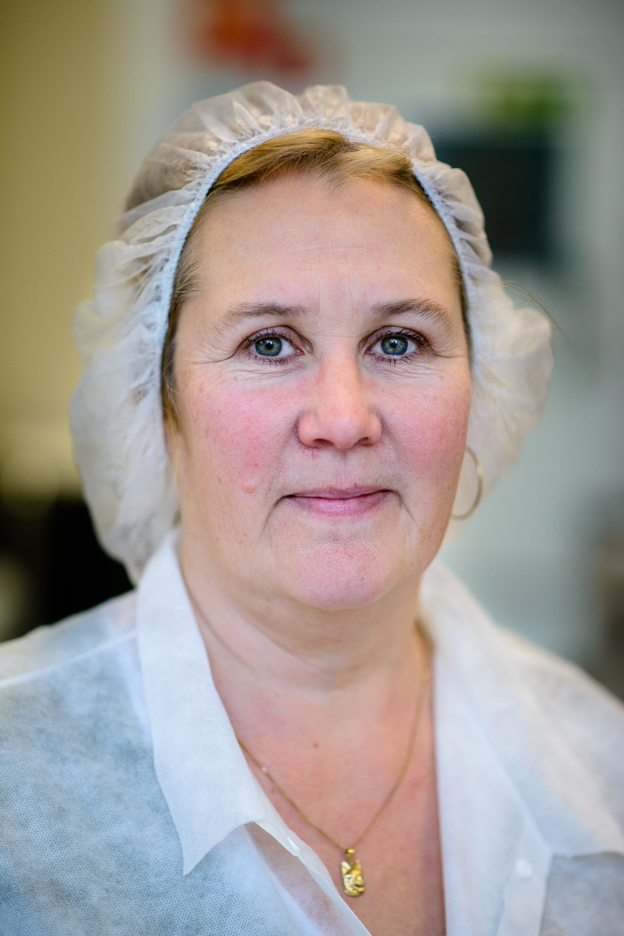 Ett porträtt på en kvinna i vit skyddsrock och hårnät i en laboratorie- eller fabriksmiljö.