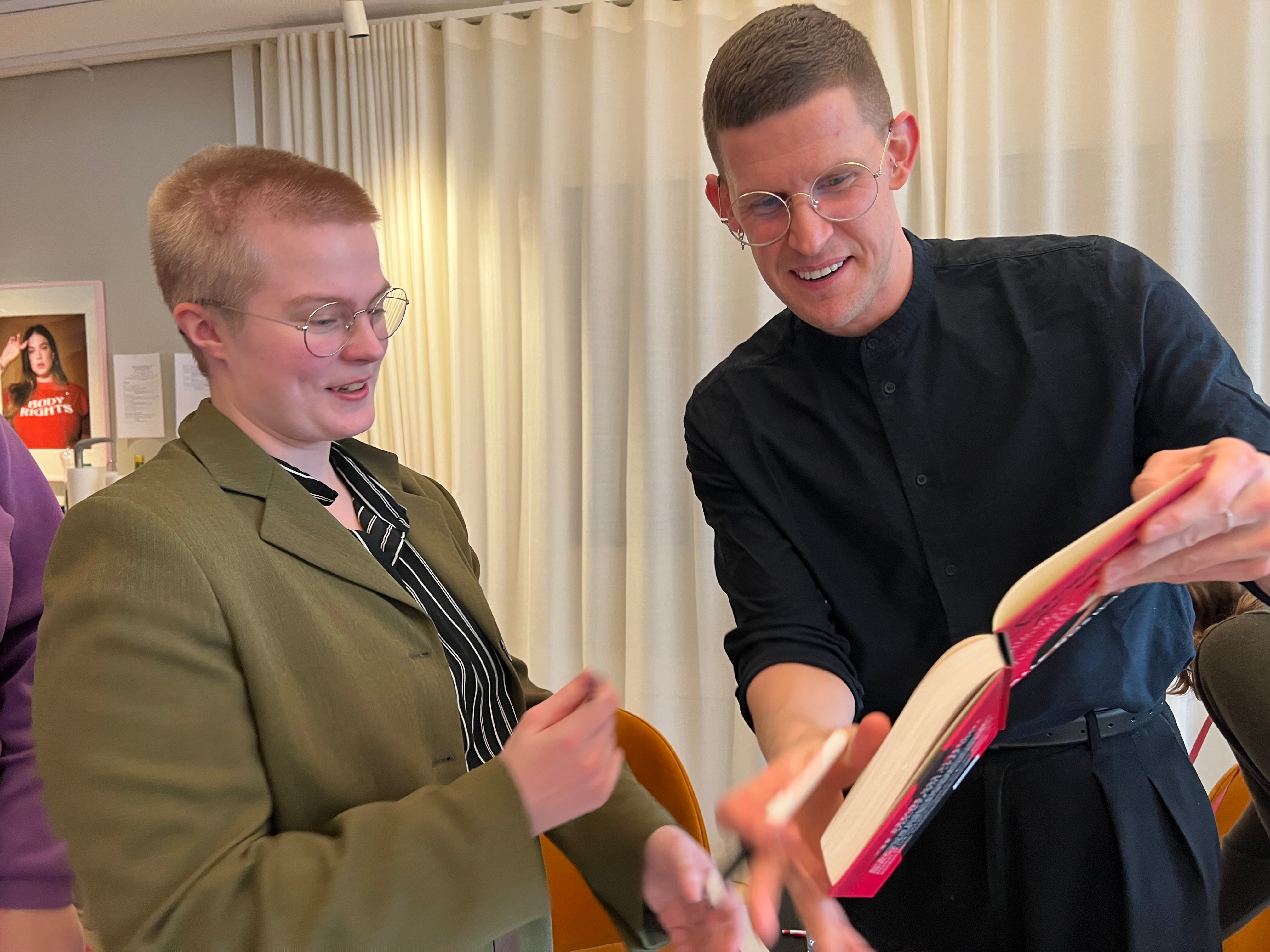 Två personer i glasögon tittar tillsammans i en bok med rött omslag.