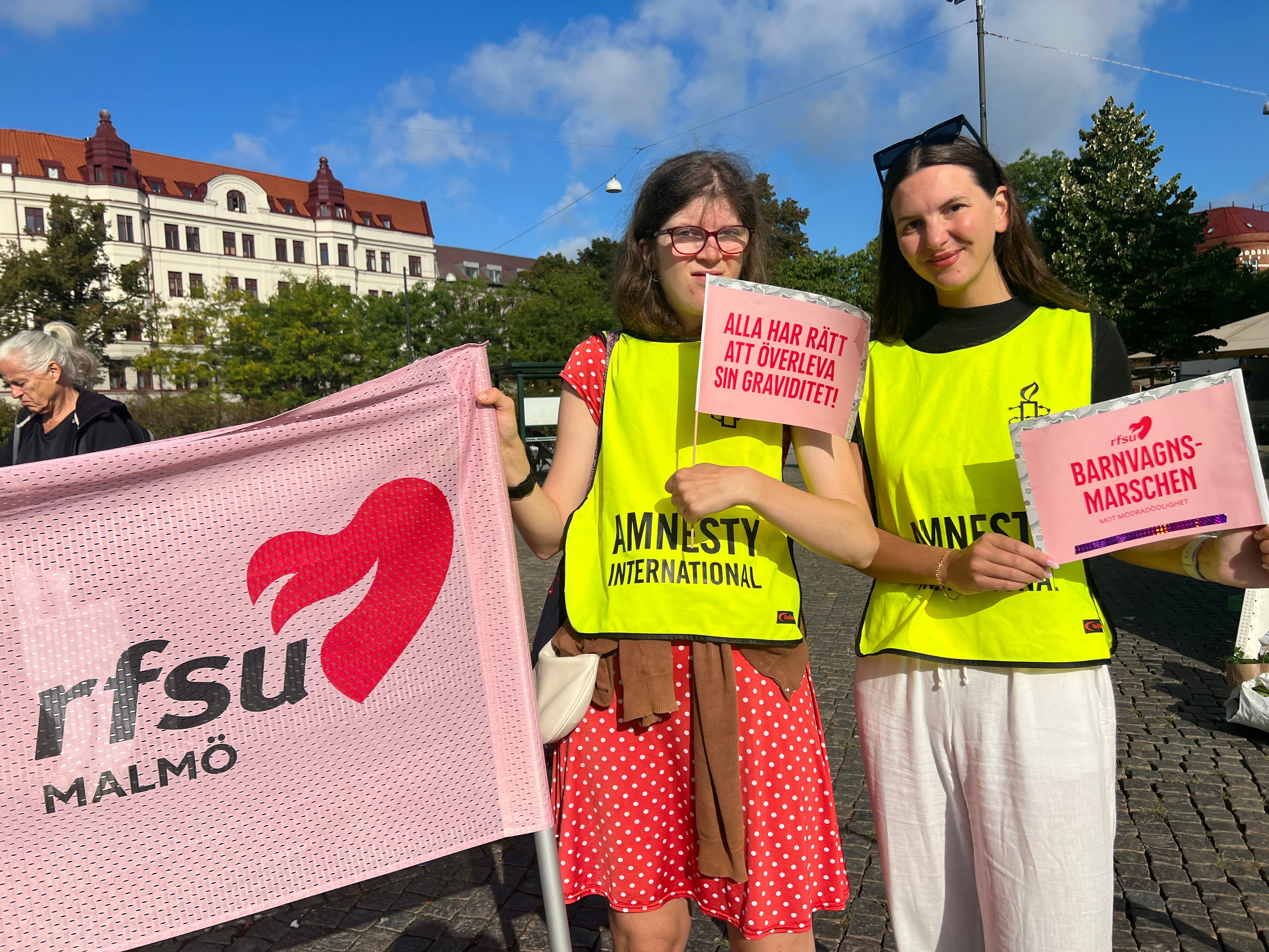 Två kvinnor står utomhus med skyltar i handen