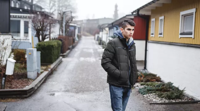 En tonårskille i dunjacka på en gata i ett villaområde 