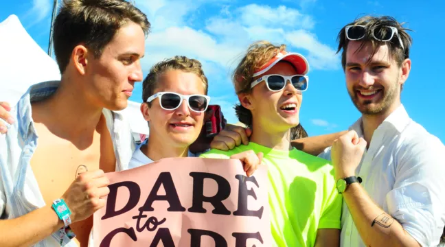 Fyra ungdomar i färgglada kläder håller upp en Dare to Care-banderoll, foto. 
