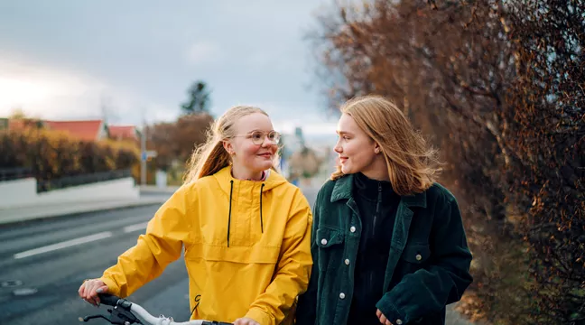 Två tonårstjejer på promenad med en cykel, foto. 