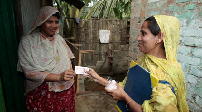 En kvinna i gul sari ger en annan kvinna en ask med preventivmedel.  