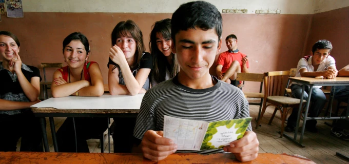 Klassrum i Georgien. En leende pojke sitter vid en skolbänk och läser en broschyr. Bakom honom sitter fyra tjejer och skrattar.  