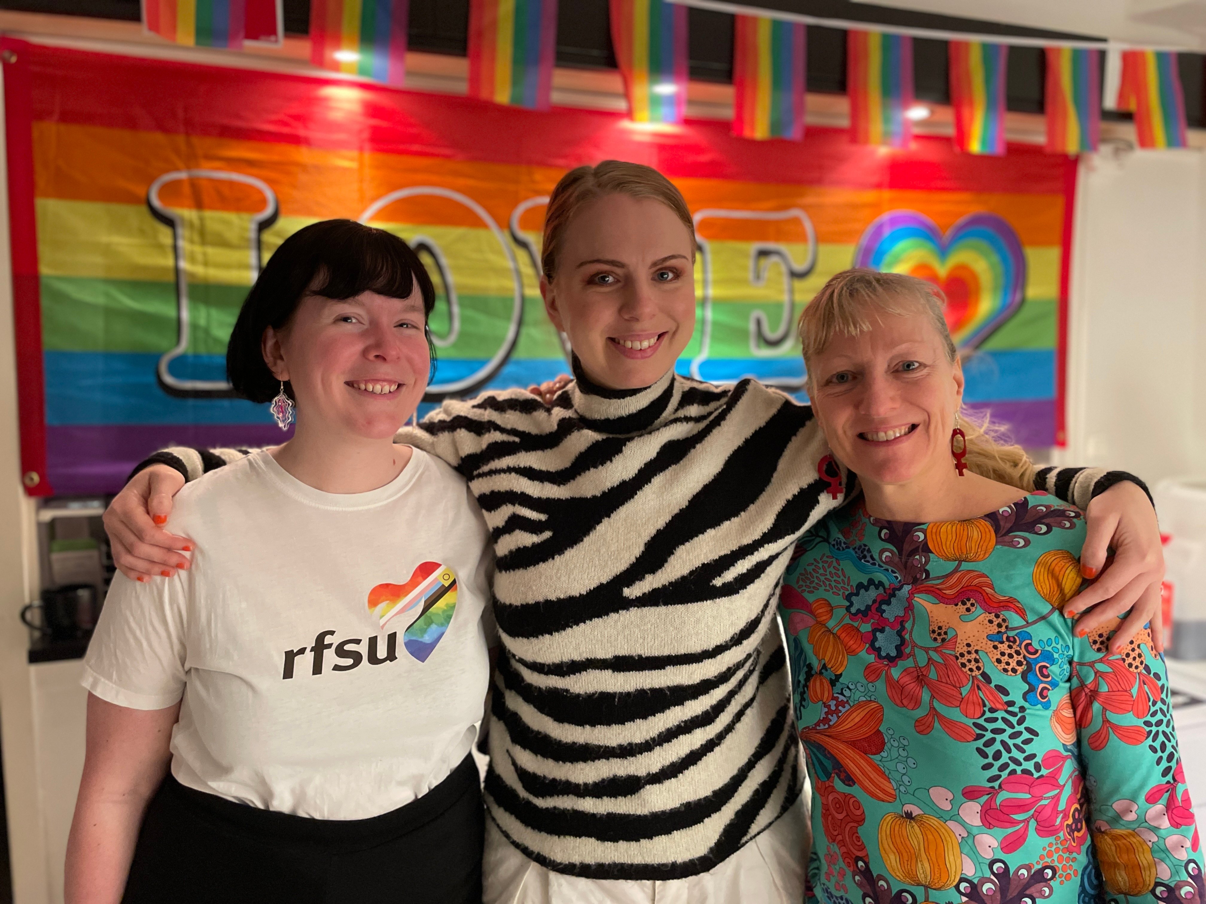 Magdalena, Berlinda och Anna från RFSU Östergötland poserar glada framför en prideflagga 