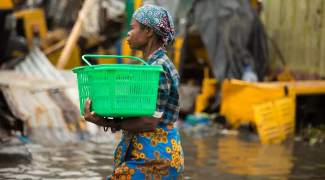 Woman walking in a flooded environment, carrying a green plastic basket. 