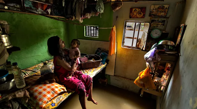 Woman sitting on the edge of a bed holding a baby. The floor is flooded.  