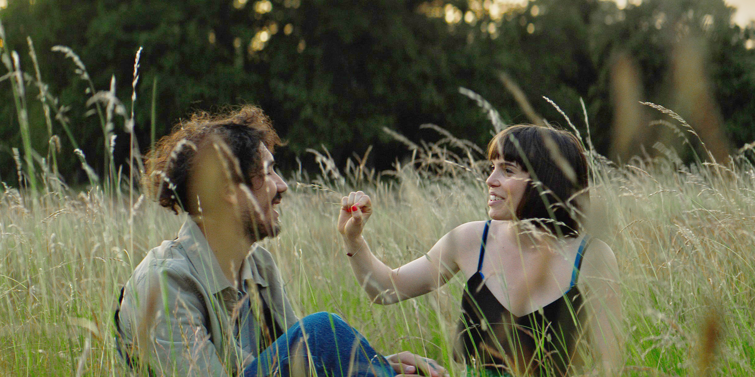 Två personer sitter på en sommaräng och ler mot varandra. Ur filmen Dear Condom 2.  