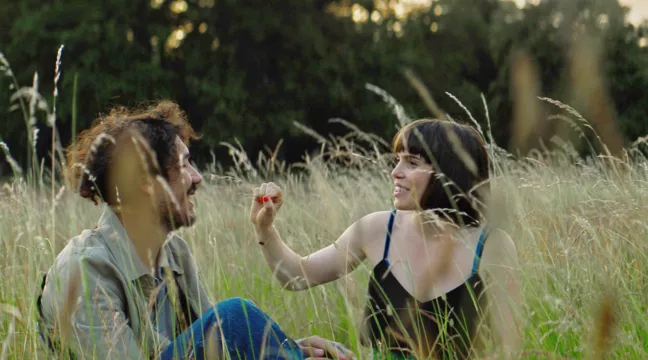 Två personer sitter på en sommaräng och ler mot varandra. Ur filmen Dear Condom 2.  