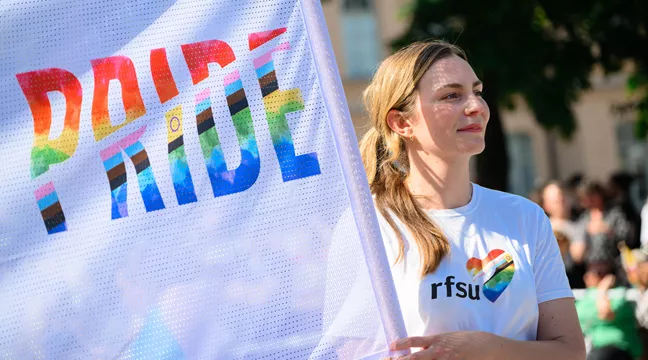 RFSU:s förbundsordförande Lina Fridén går i Prideparaden och håller i en pandelroll med texten "Pride". 