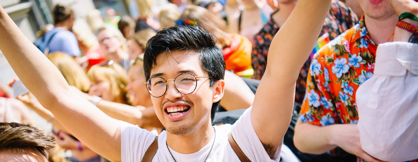 Glad person med armarna i luften under en Prideparad 