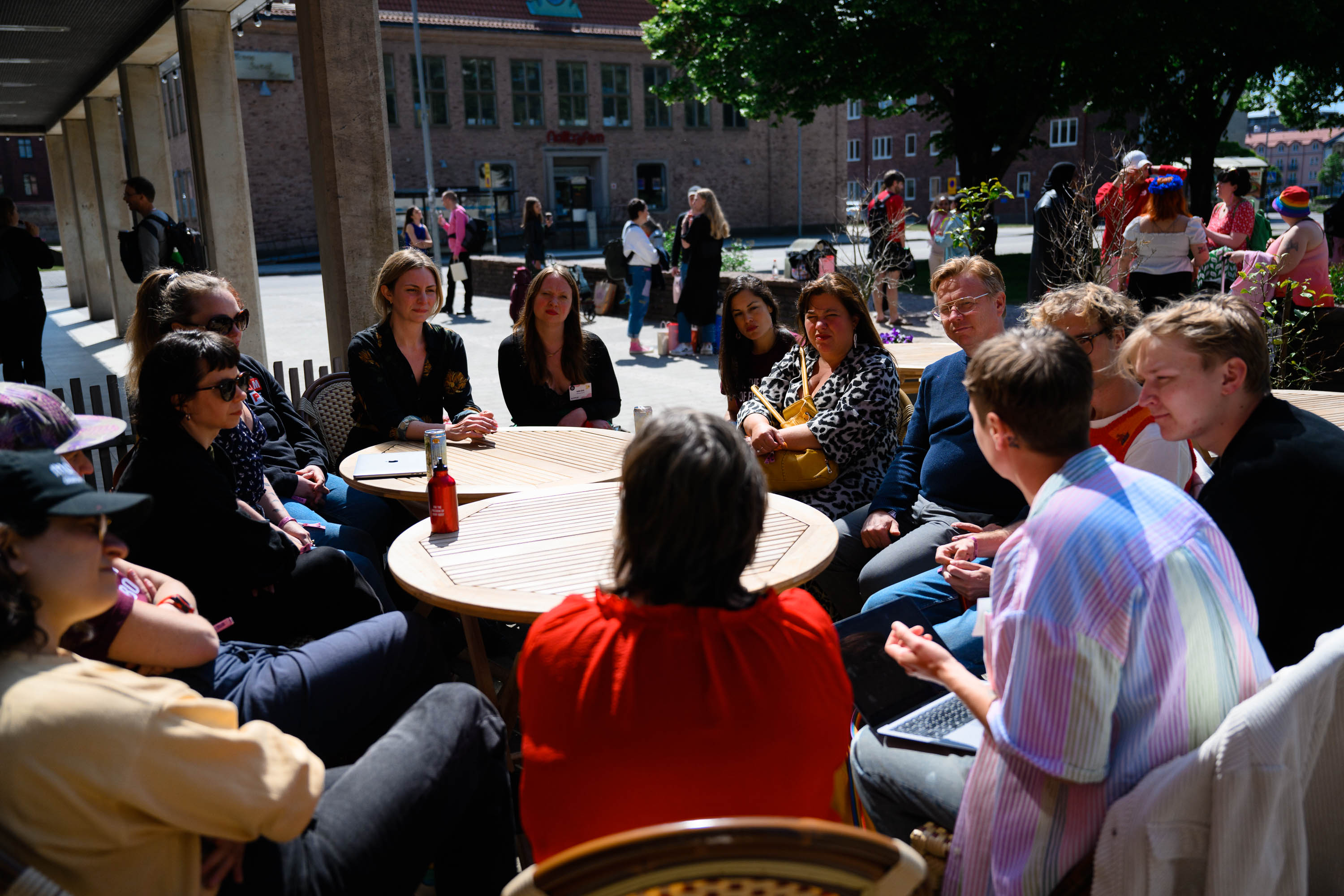 Flera personer sitter utomhus och pratar runt ett bord 