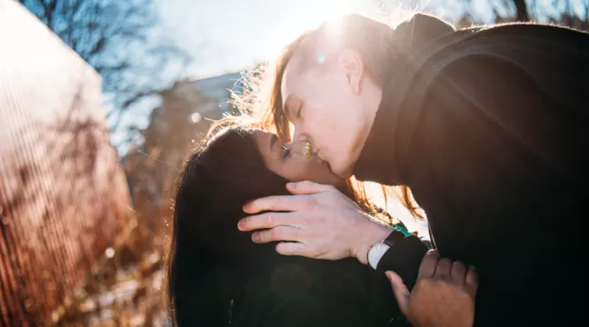 Två personer kysser varandra i solskenet. 