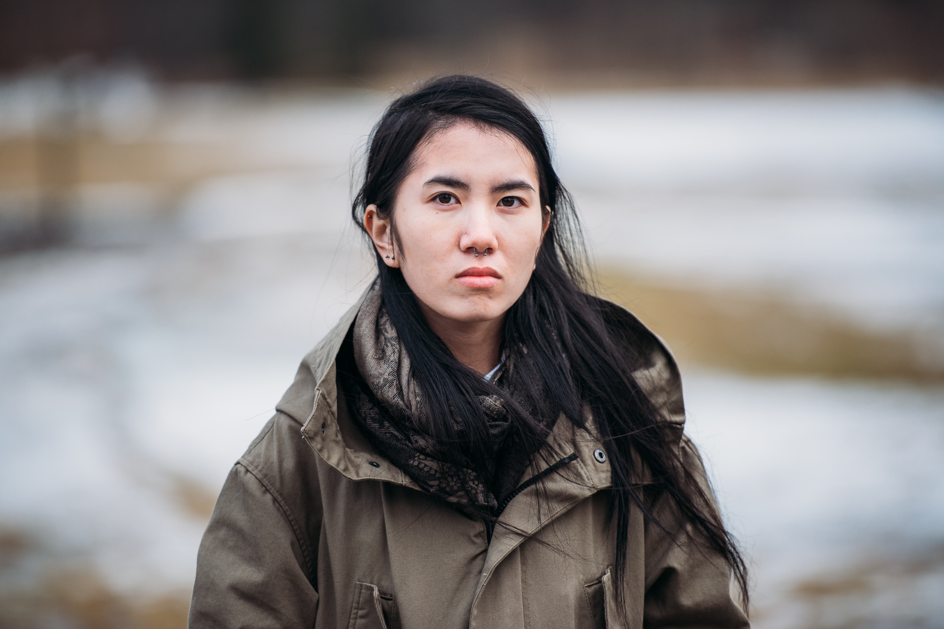 Person med långt hår och brun jacka tittar rakt in i kameran 