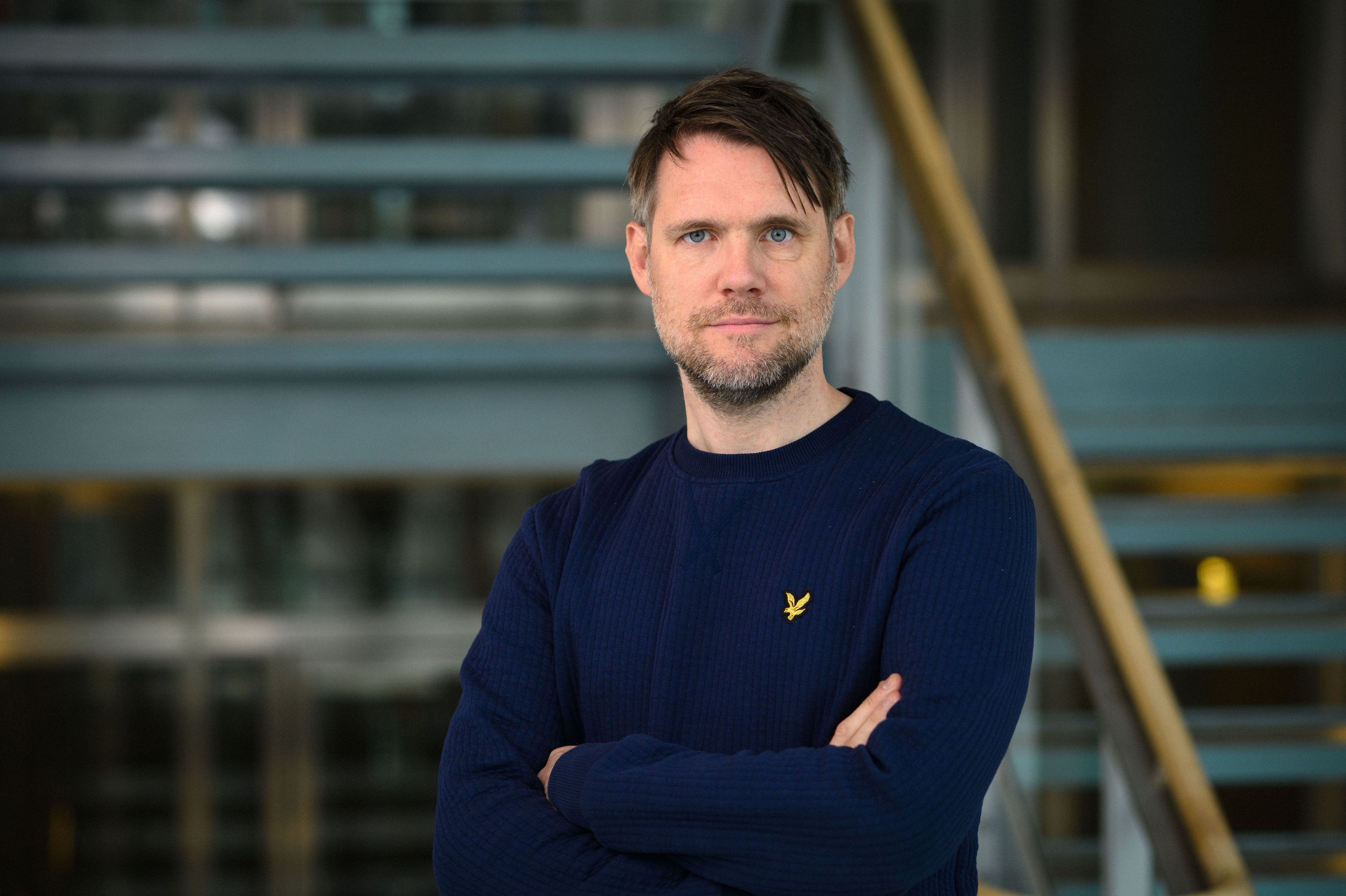 En man med marinblå tröja tittar mot kameran med armarna i kors 