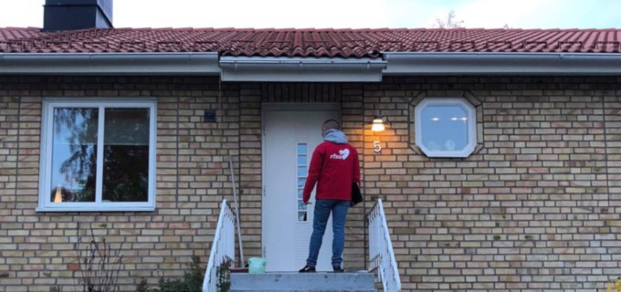 En person i röd RFSU-jacka knackar på dörren till ett hus. 