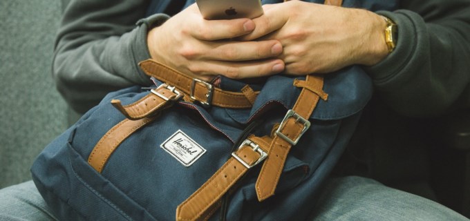 Person har ryggsäck i knäet och skrollar på sin iphone 