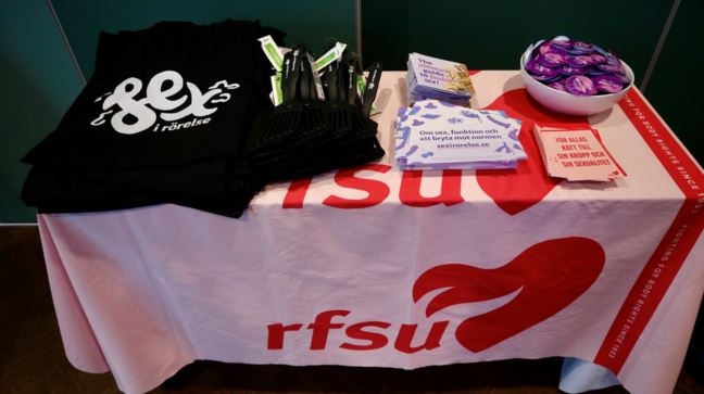 Tygväska, flyers och kondomer ligger på ett bord med RFSU-logga.  