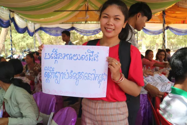En ung tjej håller upp en skylt med kambodjansk text. 
