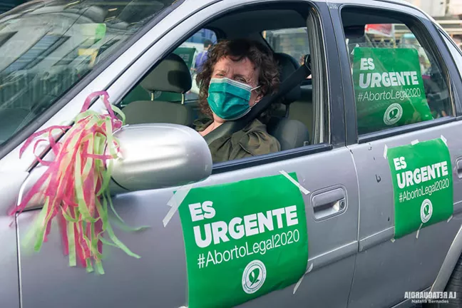 Kvinna i bil med munskydd och aborträttsplanscher utanpå bilen. 