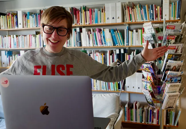 Person med glasögon gestikulerar framför en dator. 