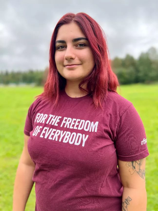 Person i halvlångt vinrött hår, iklädd vinröd t-shirt som det står For the freedom for everybody på. 