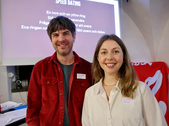 Två glada personer, en med kort hår och röd skjorta, den andra med långt hår och vit skjorta. 