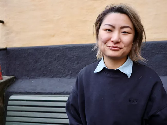 Person i mörkblå tröja, halvlångt hår och ring i näsan. 