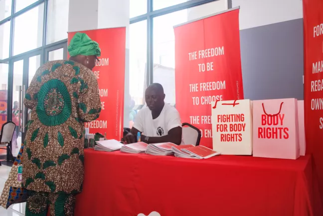En man sitter bakom ett bord. Det står "Fighting for body rights" på planscher och papperspåsar runt honom.  
