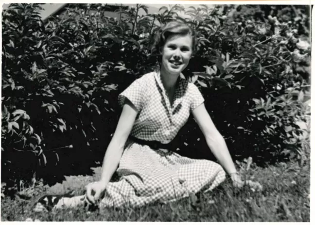 En ung person i rutig klänning sitter på en gräsmatta. 