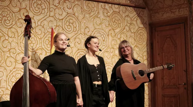 Tre personer klädda i svart tar emot applåder på en scen. 