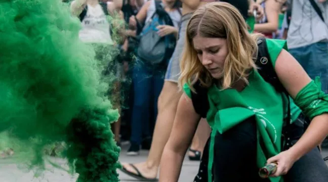 Ornella tänder en bengal med grön rök under en demonstration. 