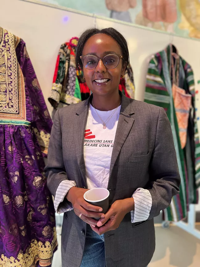 En person i kavaj och med Läkare utan gränser-t-shirt står och poserar med en kaffekopp i handen. 