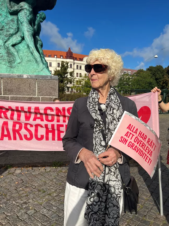 En äldre dam i solglasögon håller en vimpel i handen. 