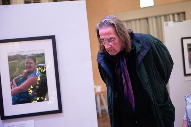 En stående person med glasögon böjer sig ner för att se en av bilderna i utställningen. 