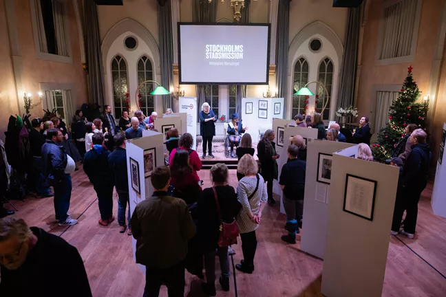 Ett foto över ett rum fullt av folk. De tittar alla på scenen där två personer befinner sig. 